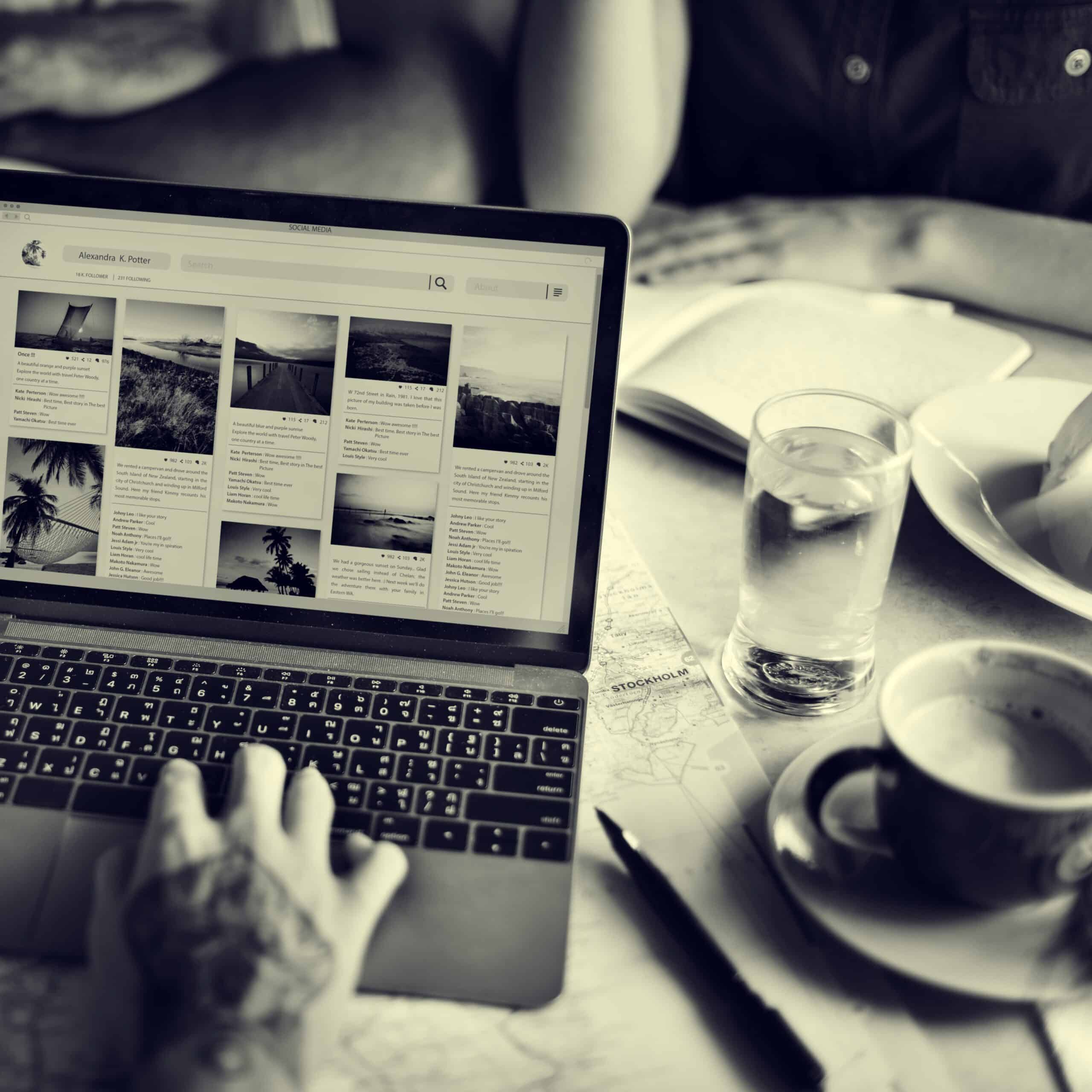 Person browsing an "About" section on a laptop in a café setting, with notebooks, coffee, and water on the table, representing storytelling and brand identity in a creative workspace.