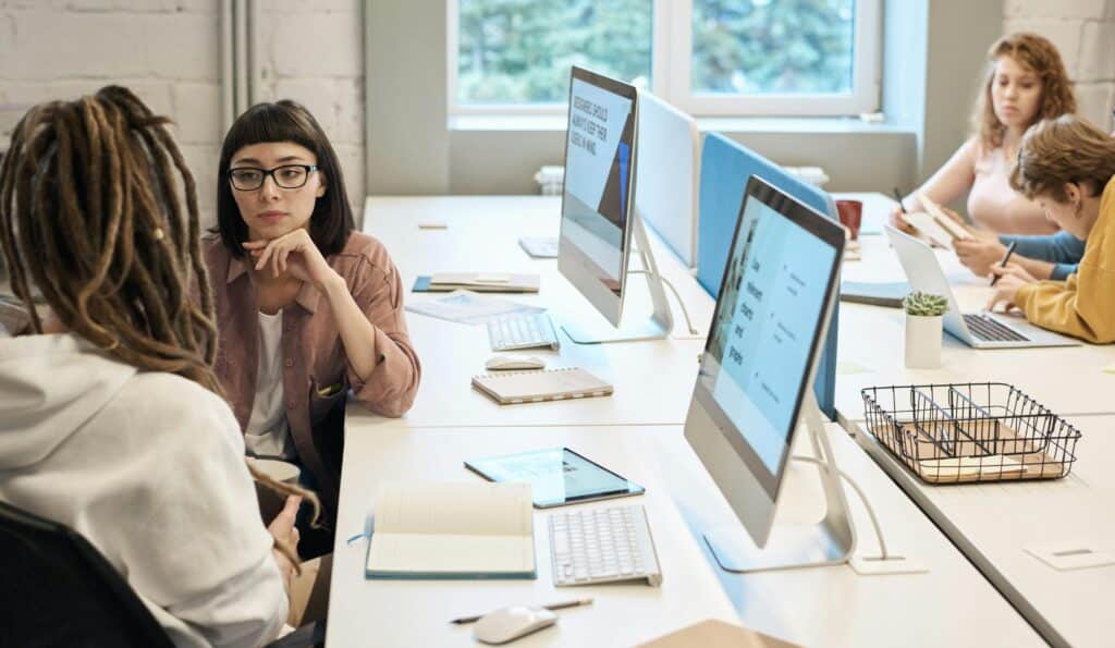 A team of professionals collaborating in a modern office with desktop computers and notebooks, discussing strategies related to SEO and digital content planning.