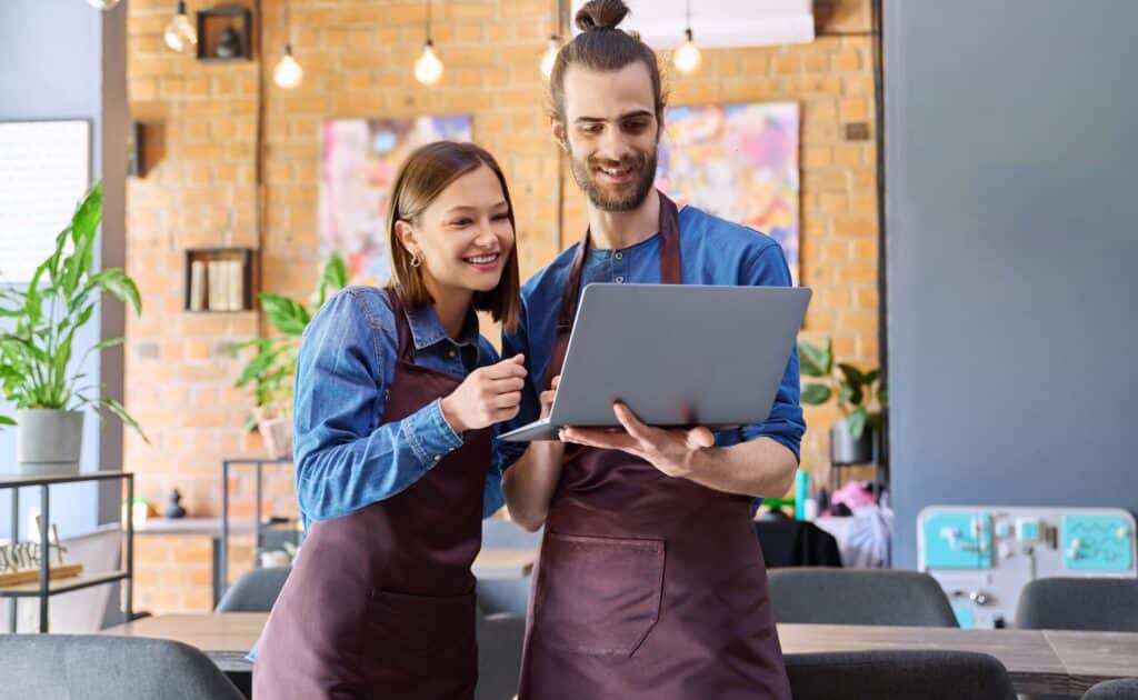 Two small business owners in aprons smiling while reviewing their website performance on a laptop, exploring SEO Auckland strategies to grow their local visibility.